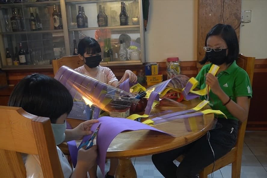 Em Lê Huỳnh Minh Khuê (bìa phải) cùng với các em trong gia đình đang làm những tấm kính chắn giọt bắn.