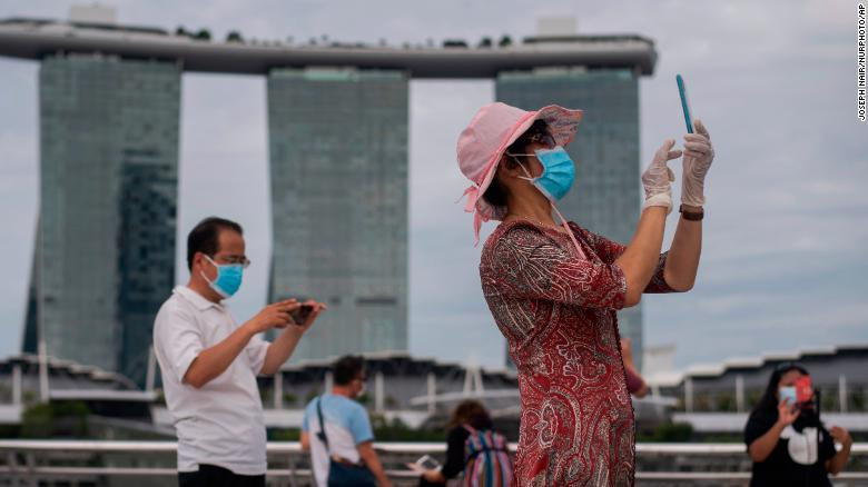 Một người phụ nữ đeo khẩu trang và găng tay chụp ảnh tại Vịnh Marina, Singapore (1/8/2021). Ảnh CNN