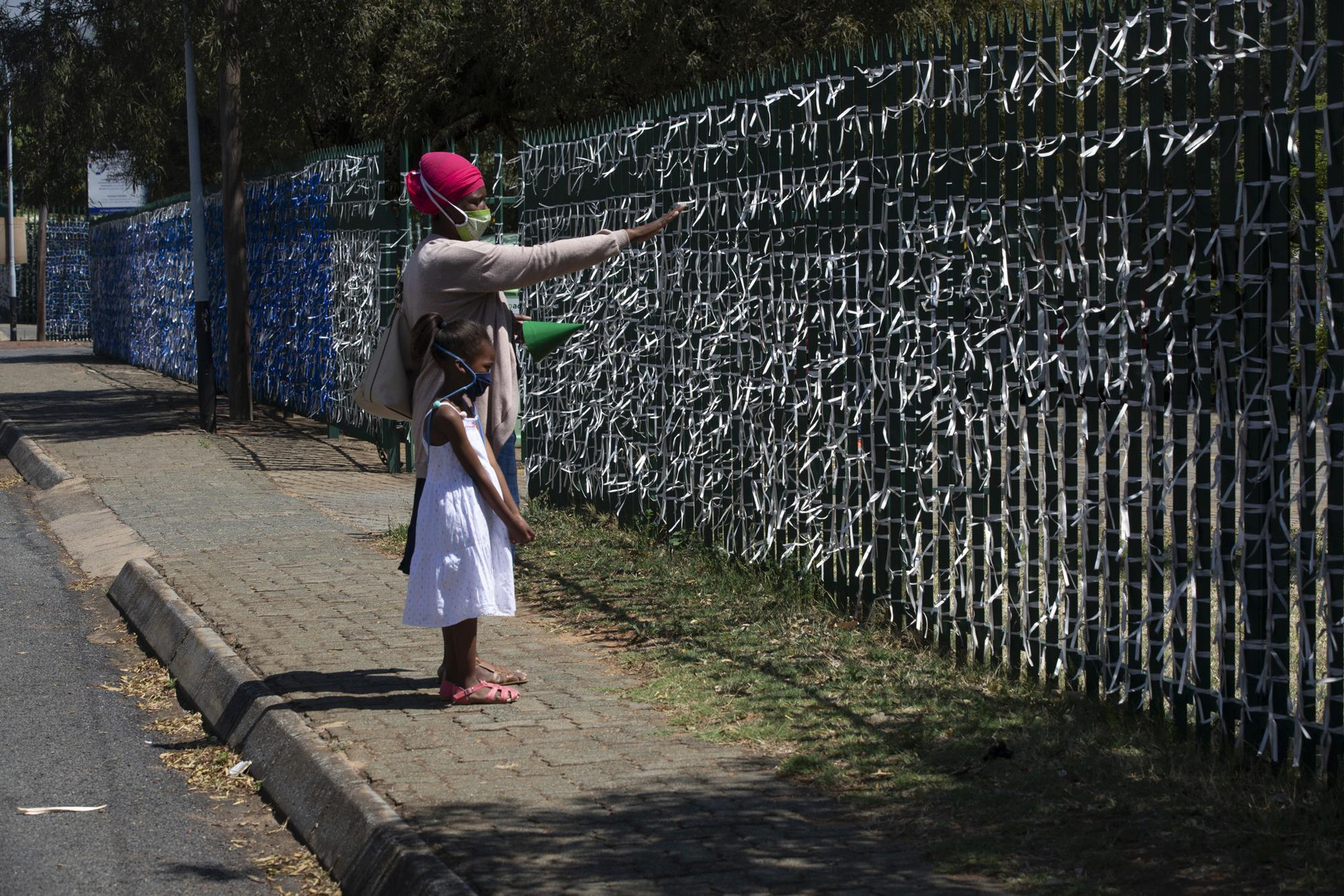 Hai mẹ con đứng trước một hàng rào treo đầy những dải ruy băng tưởng nhớ những nạn nhân của đại dịch Covid-19 tại Nhà thờ St. James Presbyterian ở Johannesburg, Nam Phi. Ảnh: AP.