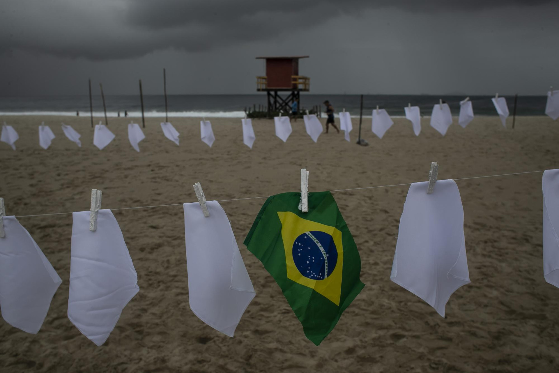 Một lá cờ Brazil được treo trên dây tại bãi biển Copacabana giữa những chiếc khăn trắng tượng trưng cho những người đã thiệt mạng do đại dịch Covid-19 ở Rio de Janeiro, Brazil. Ảnh: AP.
