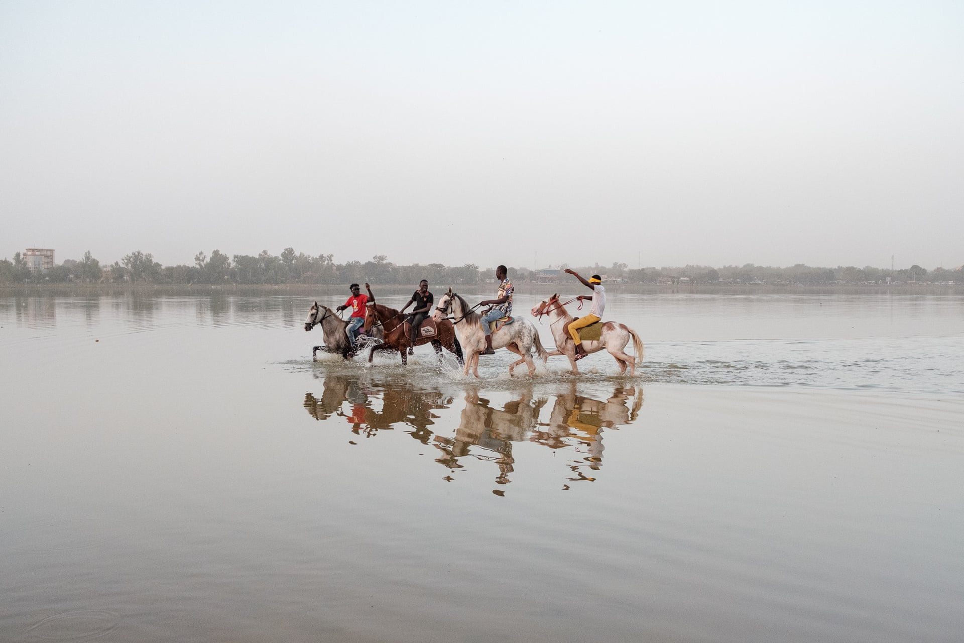 Những thanh niên trẻ đưa những con ngựa đua đi giải nhiệt trong một hồ chứa nước gần chuồng ngựa ở phía bắc thủ đô Ouagadougou, Burkina Faso. Ảnh: Guy Peterson / The Guardian.