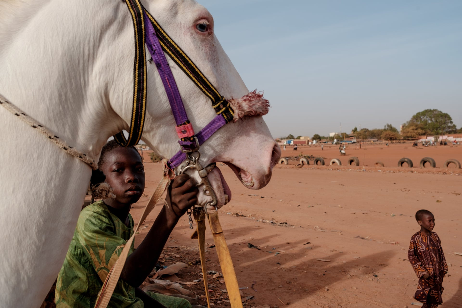 Một tay đua trẻ đứng với con ngựa của mình sau khi khởi động quanh đường đua ở Ouagadougou. Ảnh: Guy Peterson / The Guardian.