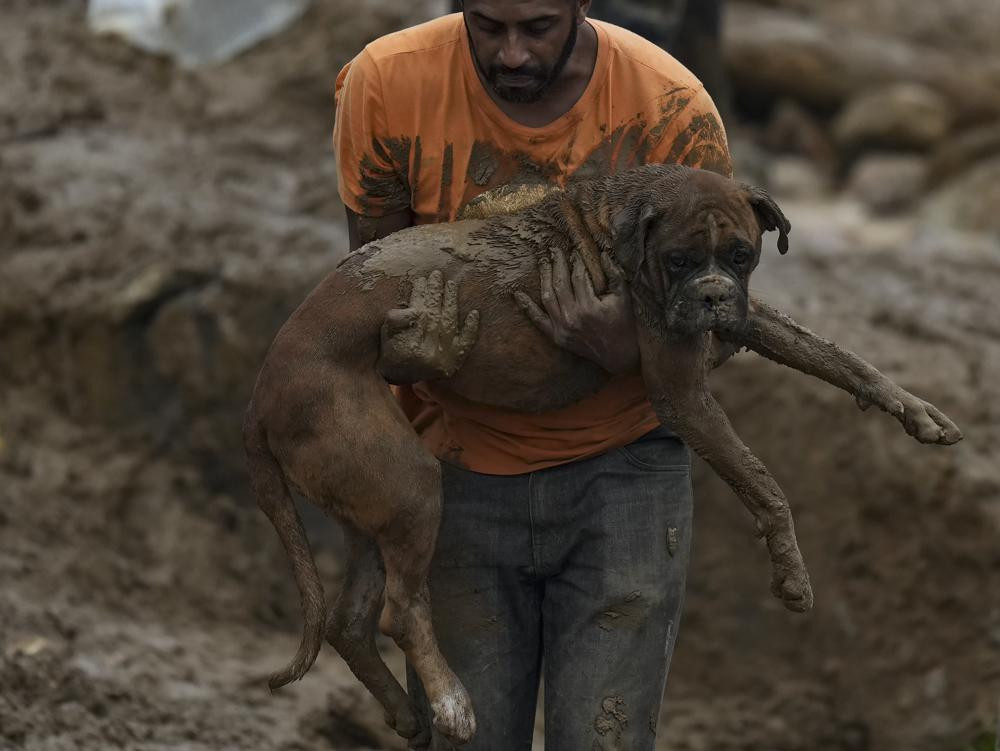 Một người đàn ông bế theo chú chó rời khỏi khu dân cư bị phá hủy do lở đất ở Petropolis, Brazil. Ảnh: AP.