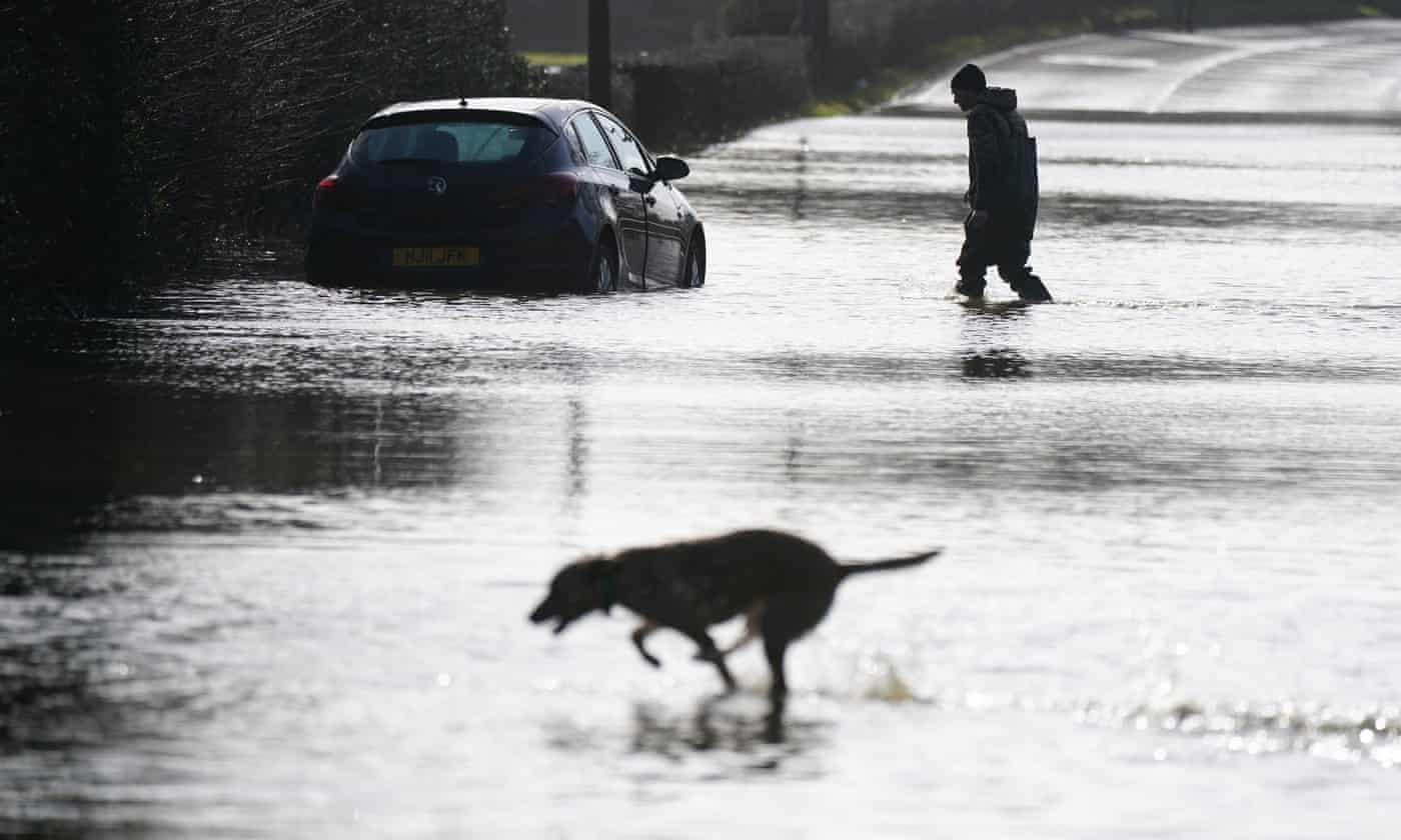 Một người đàn ông bên chiếc ô tô mắc kẹt trong nước lũ dọc đường A6 gần Milford, hạt Derbyshire. Ảnh: The Guardian.