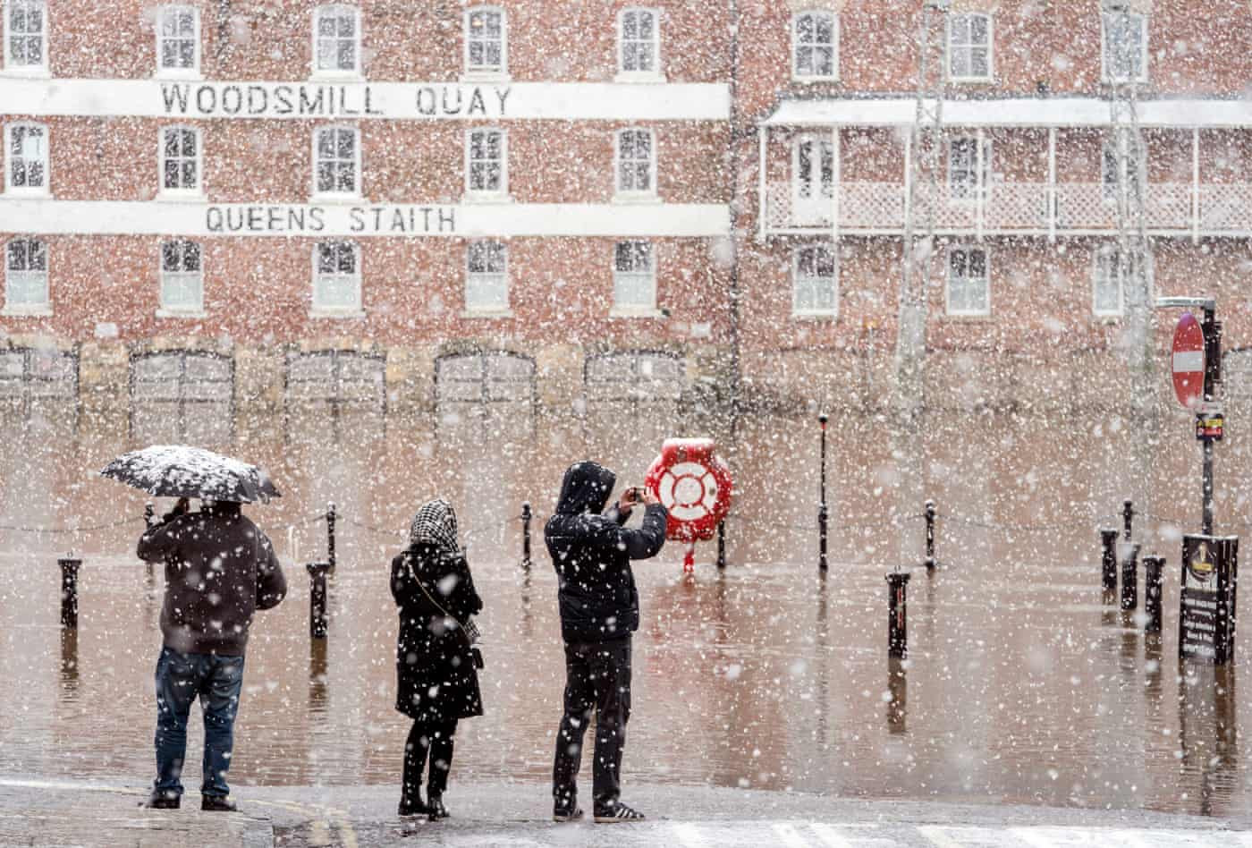 Người dân đứng nhìn dòng nước lũ giữa trận mưa tuyết sau khi cơn bão Eunice tàn phá Vương quốc Anh và Ireland. Ảnh: The Guardian.