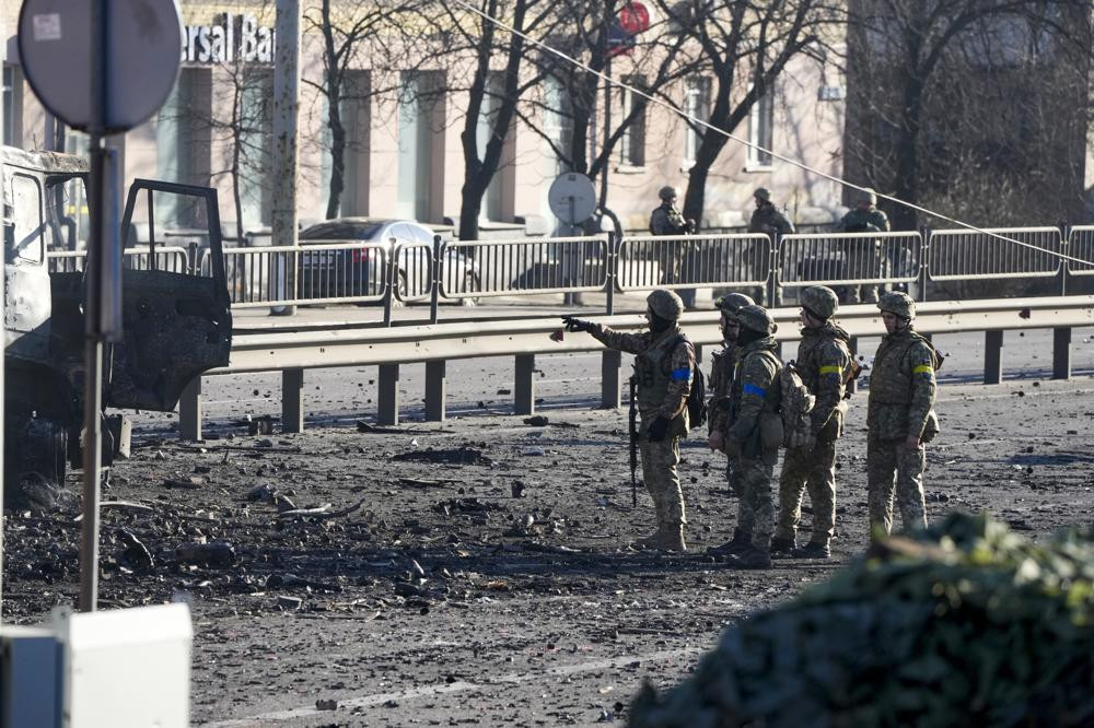 Binh sĩ Ukraine đứng cạnh mảnh vỡ của chiếc xe quân sự đang bốc cháy trên đường phố ở thủ đô Kiev sau một cuộc giao tranh ngày 26/2. Ảnh: AP.