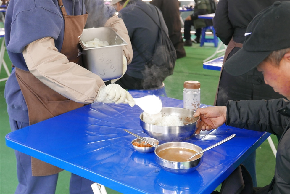 Tình nguyện viên múc thêm một muỗng cơm cho một người đàn ông tại Nhà thờ Myeongdong. Ảnh: Korea Times.