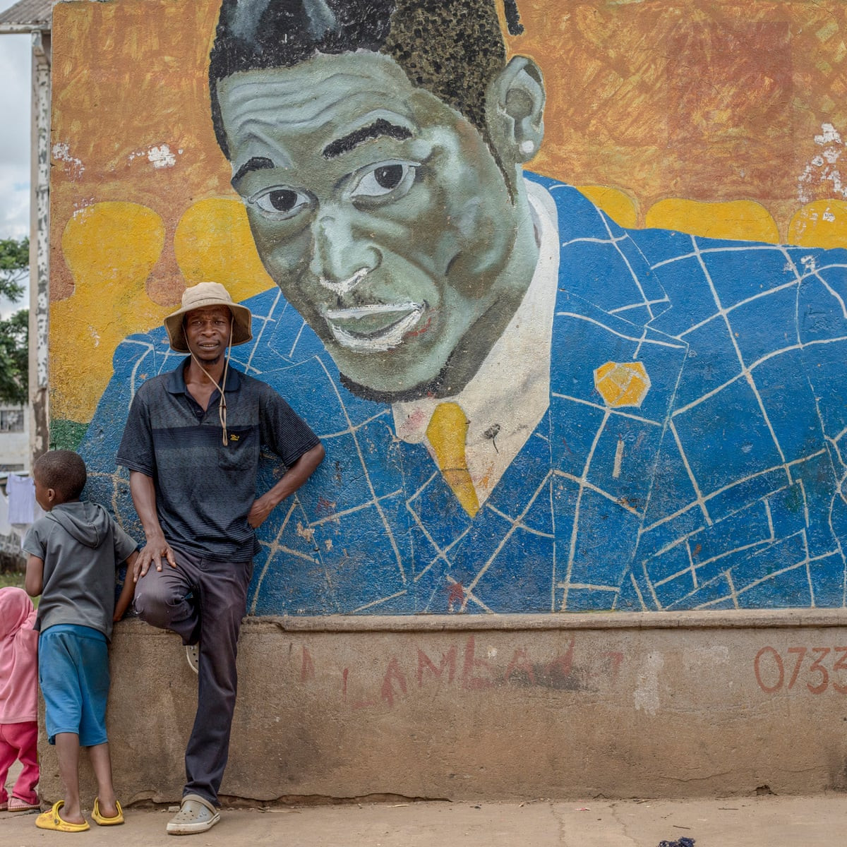 Nghệ sĩ đường phố Basil Matsika trước bức tranh tường của ông. Ảnh: The Guardian.
