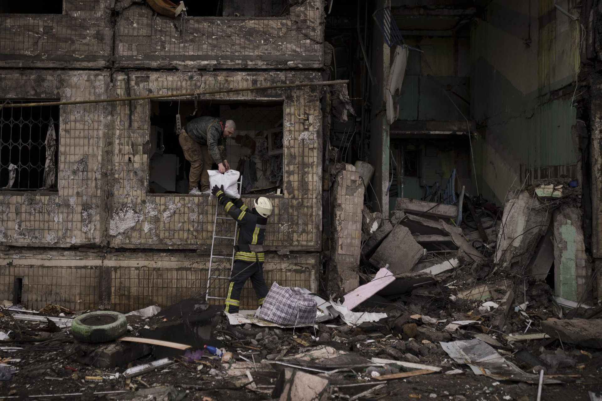 Lính cứu hỏa giúp một người đàn ông dọn đồ đạc khỏi tòa nhà bị phá hủy ở thủ đô Kiev, Ukraine. Ảnh: AP.