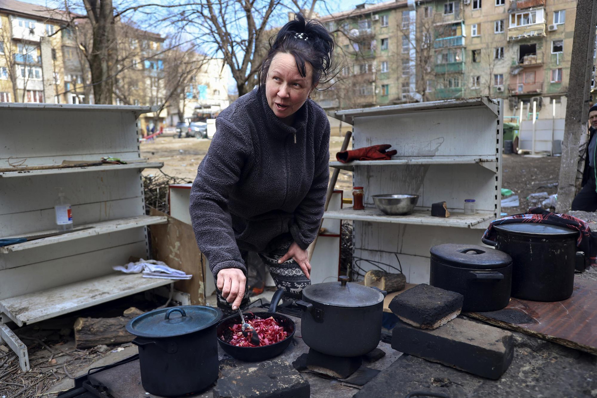 Một phụ nữ nấu ăn trong sân các tòa nhà chung cư bị hư hại ở ngoại ô Mariupol, Ukraine. Ảnh: AP.