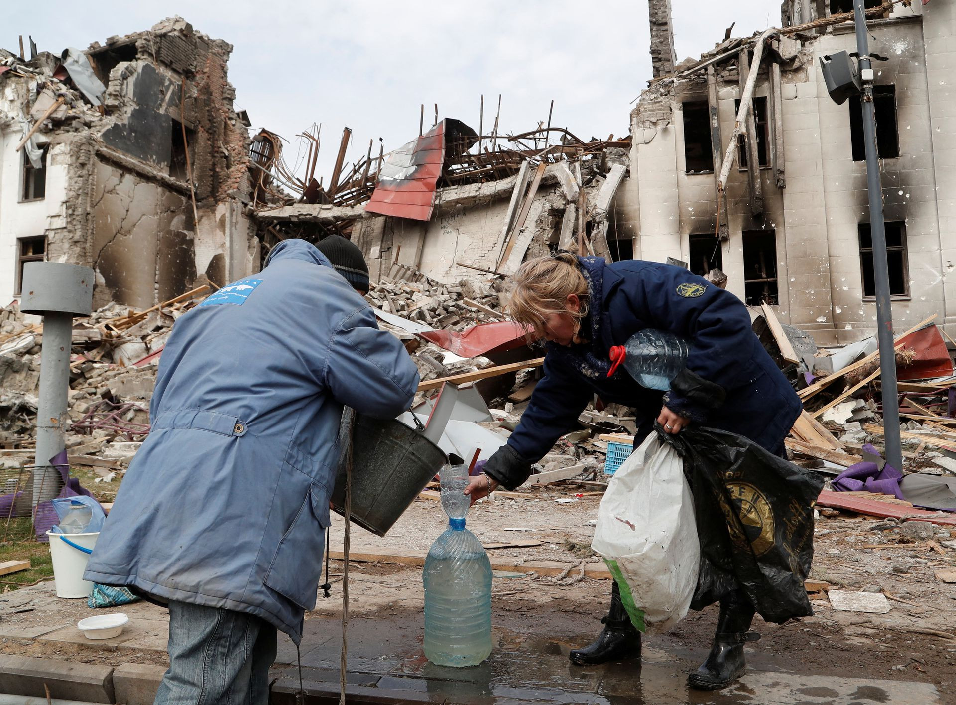 Người dân lấy nước từ một giếng gần một nhà hát bị phá hủy ở Mariupol, Ukraine. Ảnh: AP.