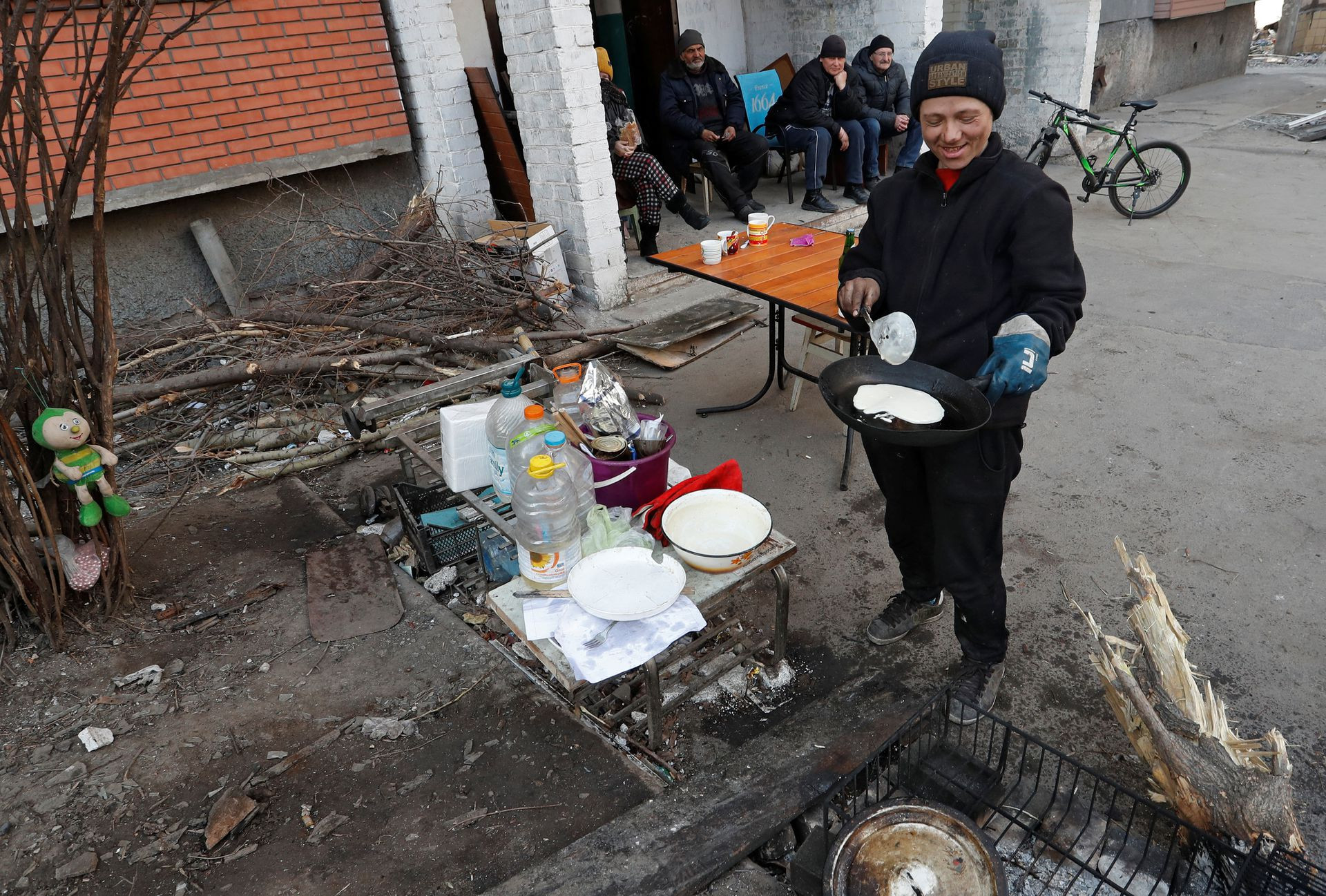 Cư dân địa phương nấu bánh kếp bên ngoài một tòa nhà chung cư ở Mariupol, Ukraine. Ảnh: AP.