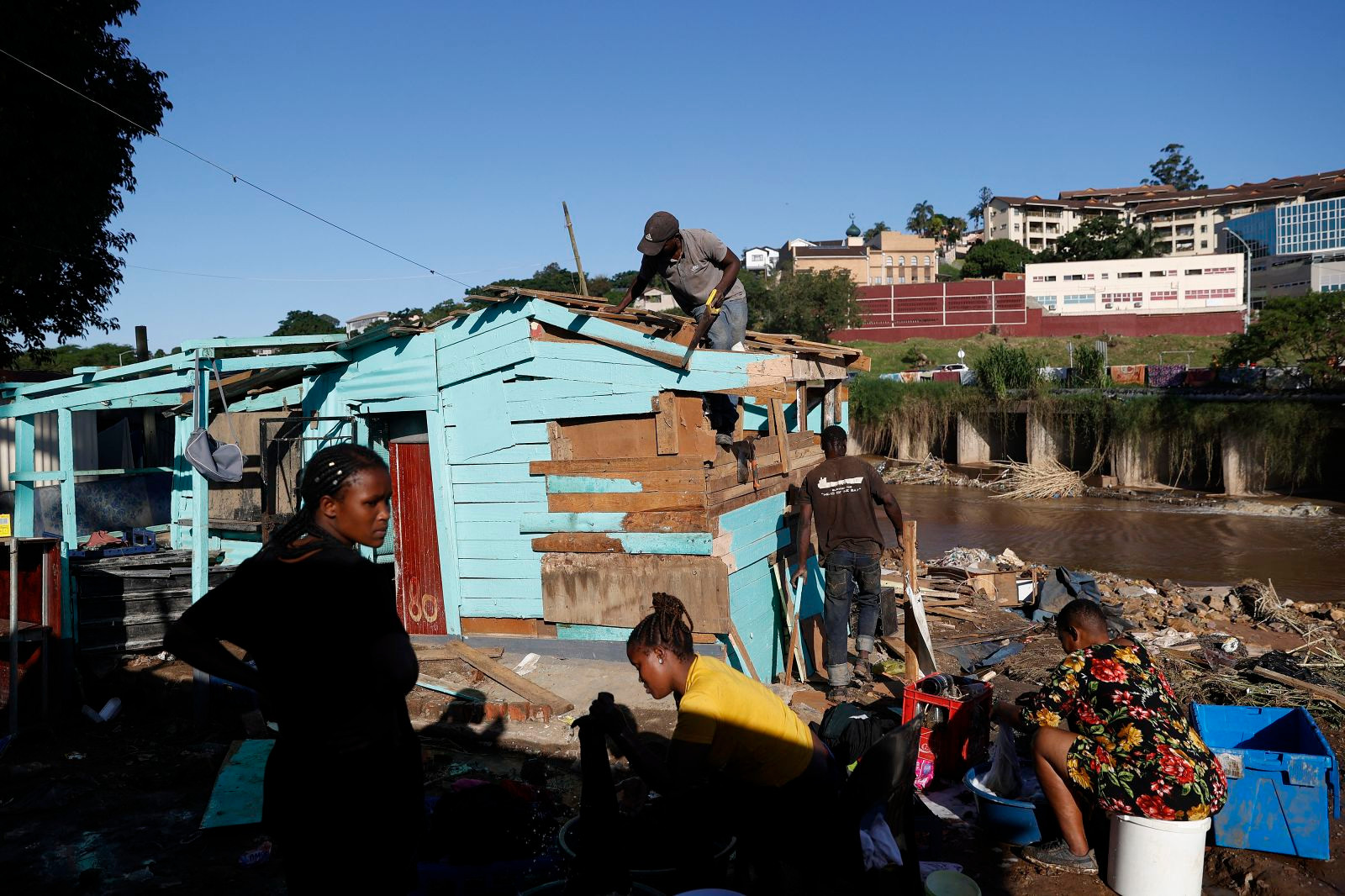 Một vài người giặt quần áo trong khi những người khác làm việc để xây dựng lại các ngôi nhà bị hư hỏng ở Durban. Ảnh: CNN.