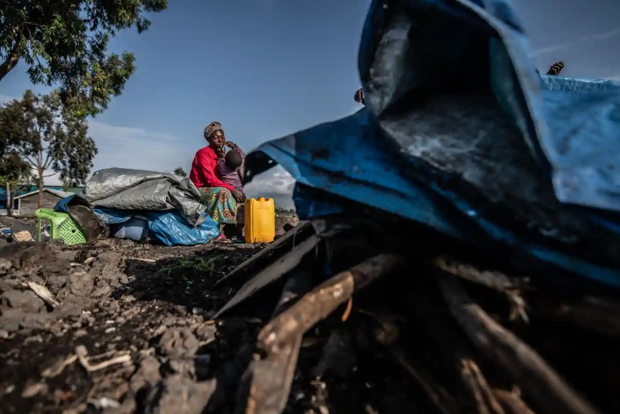 Cô Consolata Kabugho, 30 tuổi, ngồi với con bên ‘ngôi nhà tạm’ đã tháo dỡ để chuẩn bị cho việc chuyển đến một nơi trú ẩn công cộng gần đó. Ảnh: The Guardian.