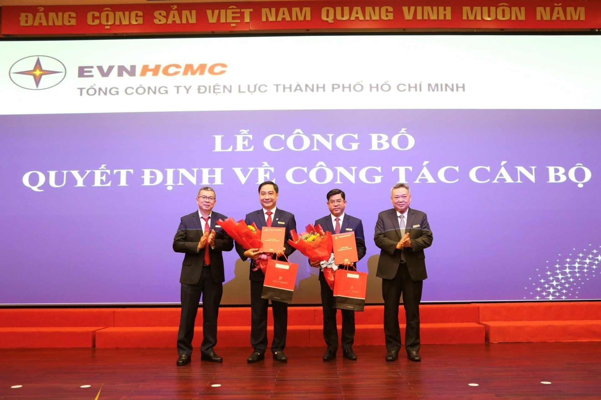 Ông Bùi Hải Thành và ông Nguyễn Thanh Nhã nhận quyết định và hoa chúc mừng từ Chủ tịch EVNHCMC Phạm Quốc Bảo (bìa phải) và Tổng giám đốc EVNHCMC Nguyễn Văn Thanh (bìa trái).