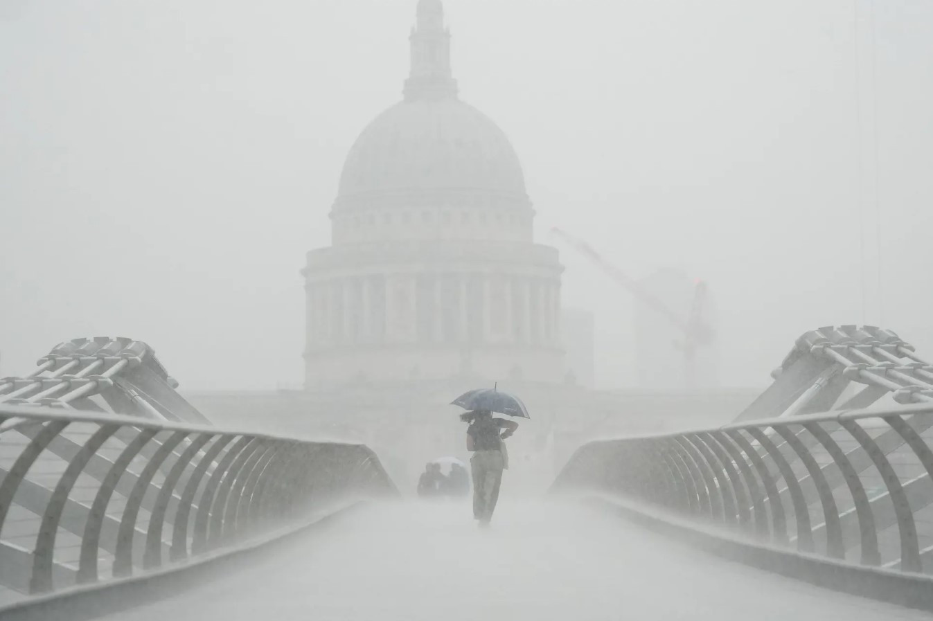 Những người cầm ô đi dưới mưa trên cây cầu Millennium. Sau nhiều tuần thời tiết oi bức, Met Office đã đưa ra cảnh báo giông bão khi mưa xối xả đổ bộ vào các vùng của Anh và xứ Wales. Ảnh: Victoria Jones / PA.