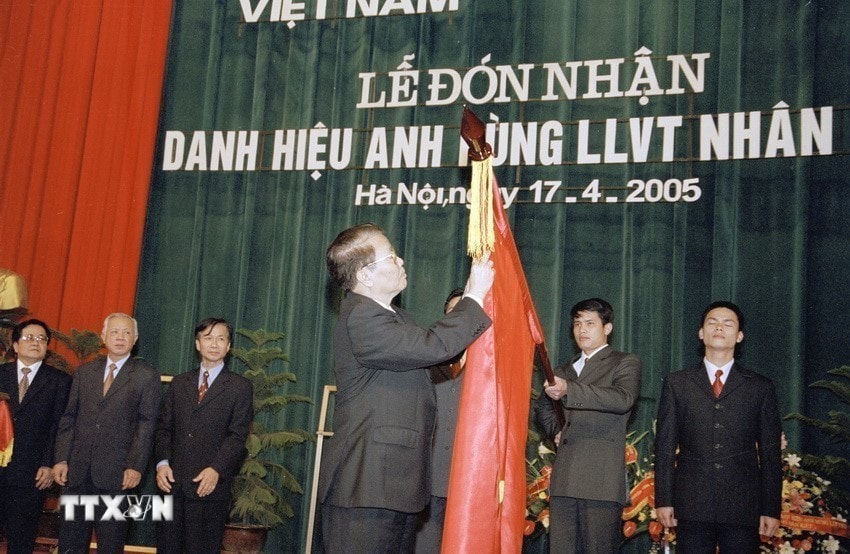 Chủ tịch nước Trần Đức Lương gắn huy hiệu Anh hùng Lực lượng vũ trang nhân dân lên lá cờ truyền thống của Thông tấn xã Việt Nam, ngày 17/4/2005. (Ảnh: Nguyễn Khang/TTXVN)